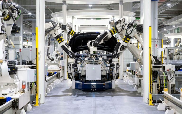 Robotic arms assembling a car in a modern factory, illustrating automation’s role in manufacturing wage trends.